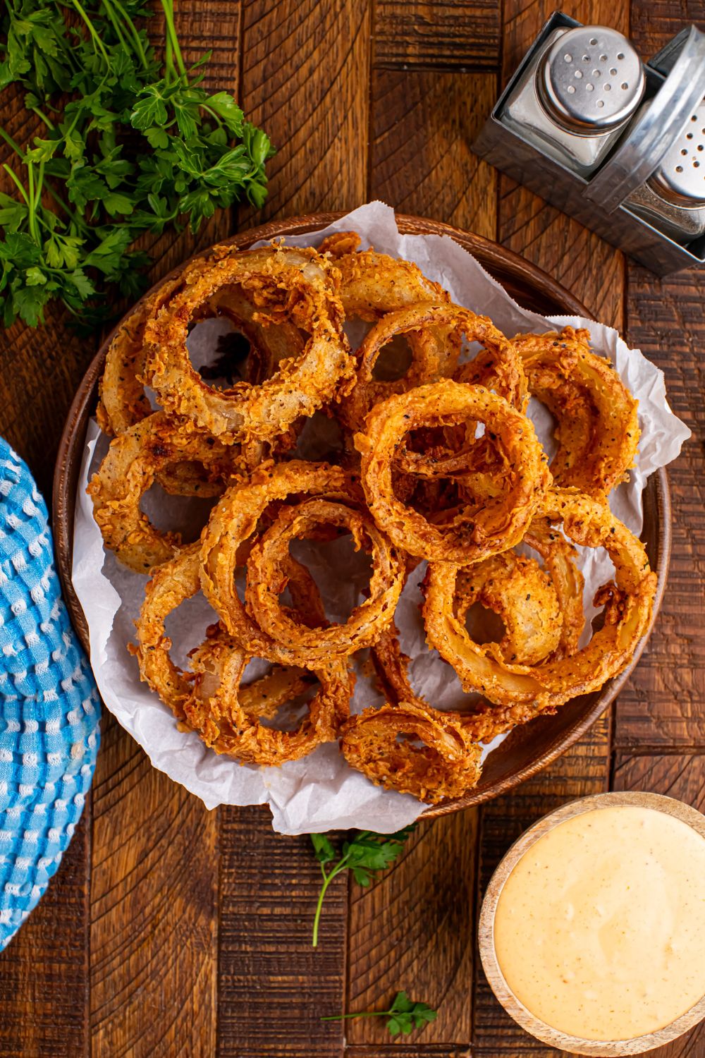 overhead look of table with Homemade Deep Fried Onion Rings in a bowl and sauce, salt, and pepper on table as well 