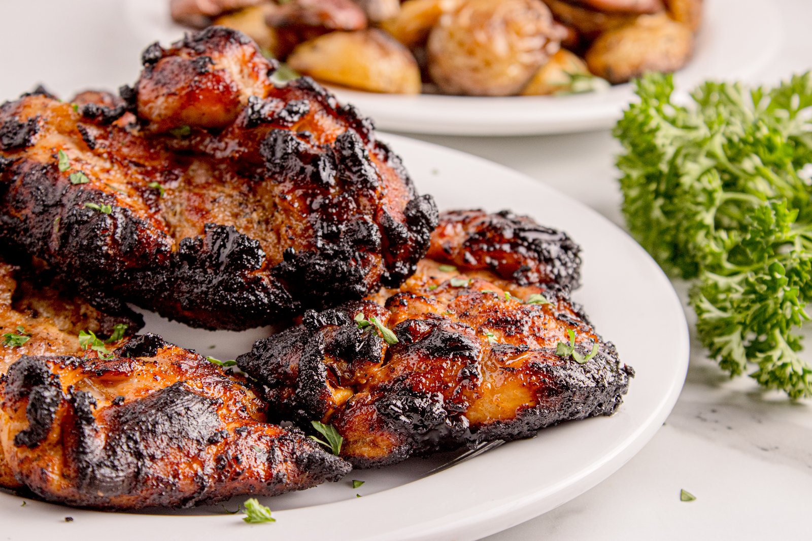 Grilled Chicken Thighs on a plate with roasted potatoes behind on another plate