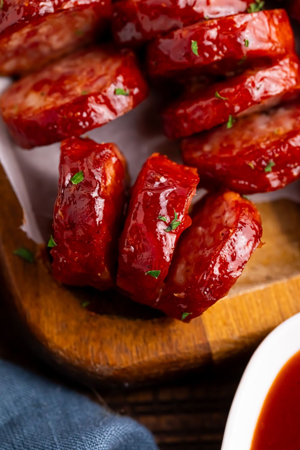 close up of BBQ Hasselback Smoked Sausages on a wooden cutting board with a side of sauce 