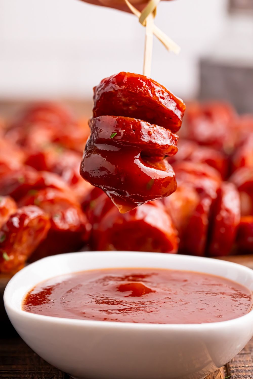 BBQ Hasselback Smoked Sausages dipped in sauce being held above the bowl 