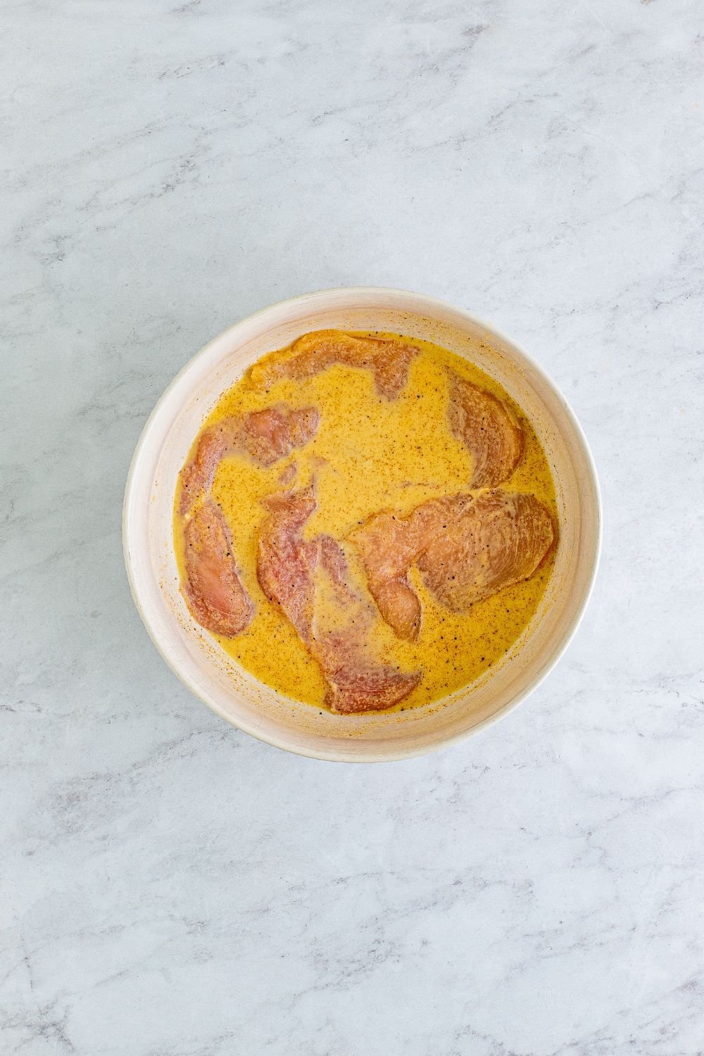 chicken breasts in a bowl with pickle juice and milk on table