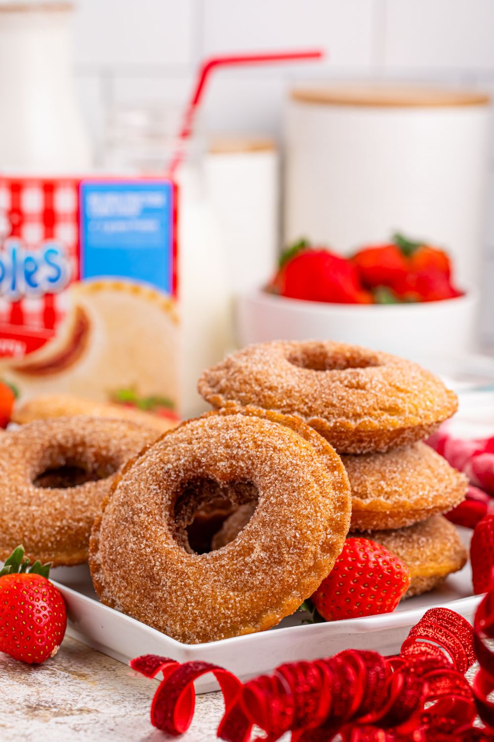 Fried Strawberry Uncrustables stacked on plate and placed around with some strawberries in a bowl behind plate and a glass of milk with straw 