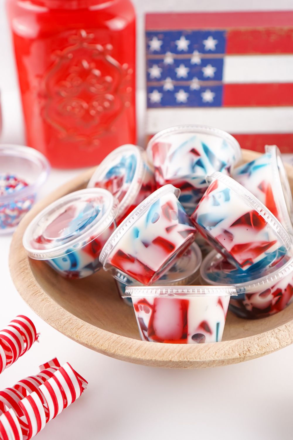 Red White and Blue Jello Shots in a bowl on table with American flag in background 