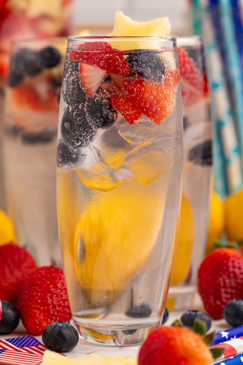 Patriotic Sparkling Lemonade in glasses topped with fruit in each glass. Fruit is scattered on table 