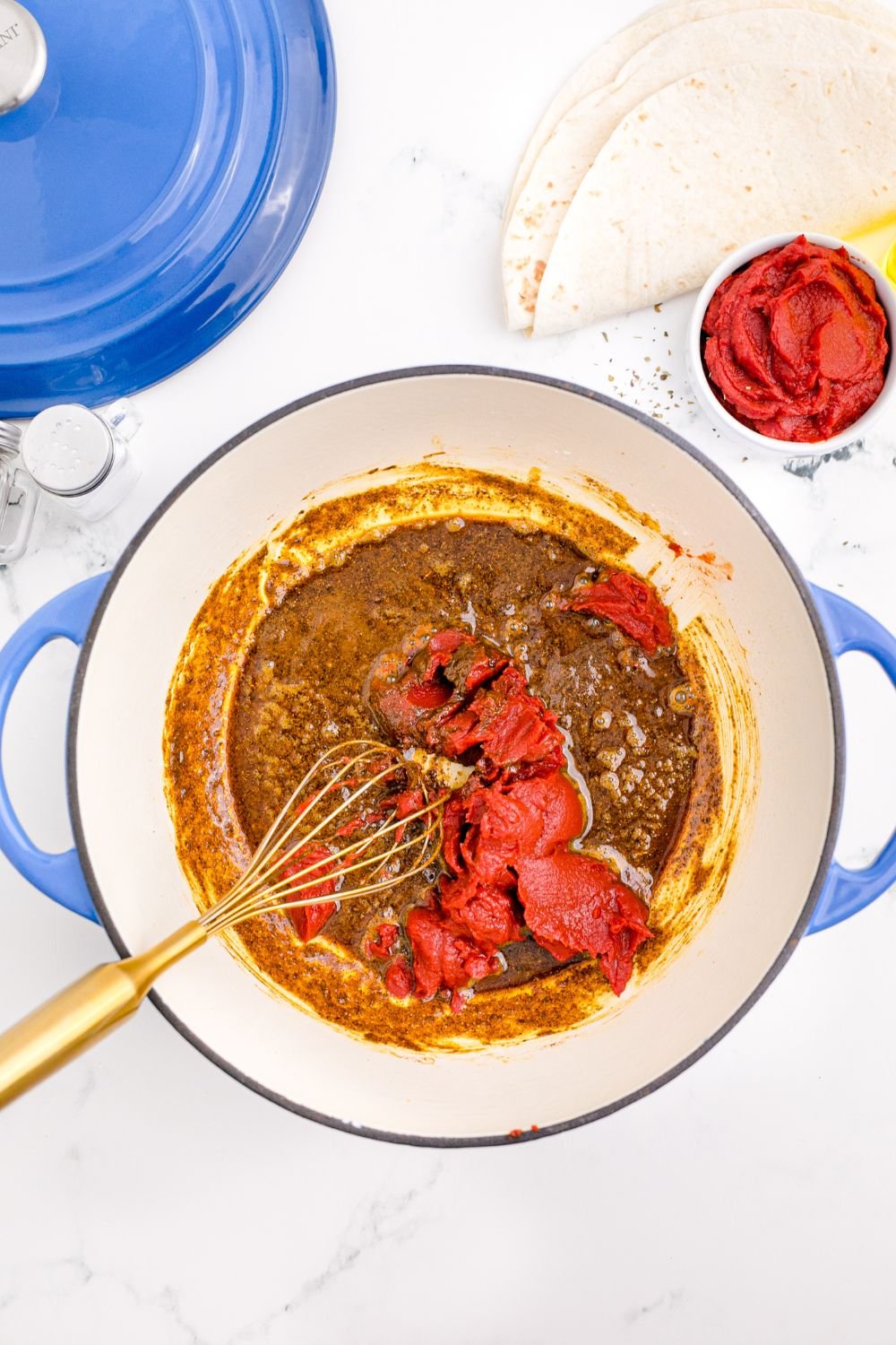a whisk mixing up tomato paste in a pot on table for making Homemade Enchilada Sauce