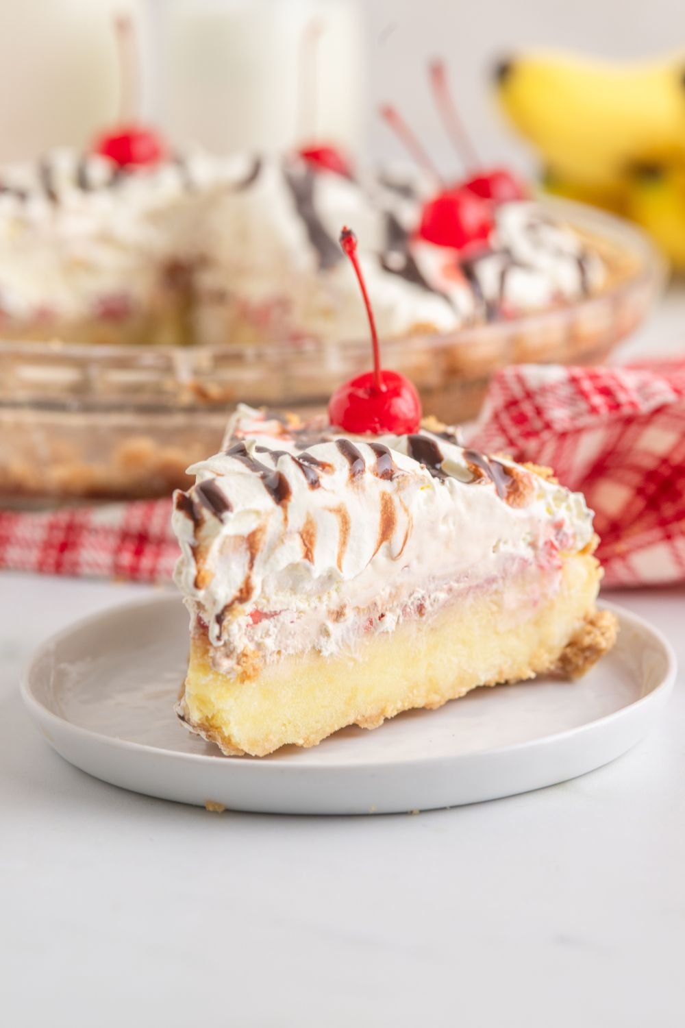 No Bake Banana Split Pie on table with a slice placed on a plate 