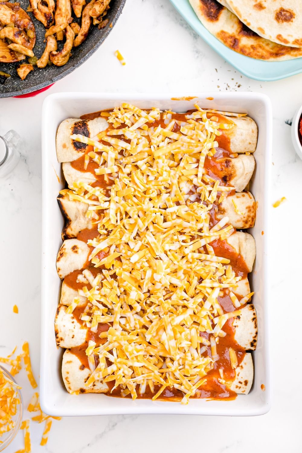 uncooked Cheesy Chicken Enchiladas sitting in casserole pan on table 