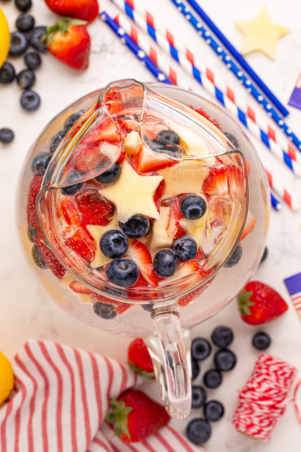 glass pitcher with Patriotic Sparkling Lemonade in it, and topped with star shaped apples, blueberries and strawberries