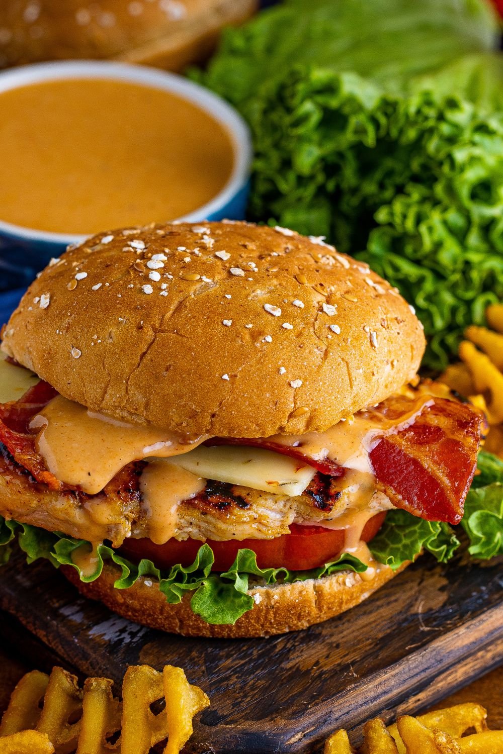 view of sandwich on table to show chicken, bacon and more on the Chick Fil A Grilled Chicken Sandwich with lettuce and fries scattered around it 