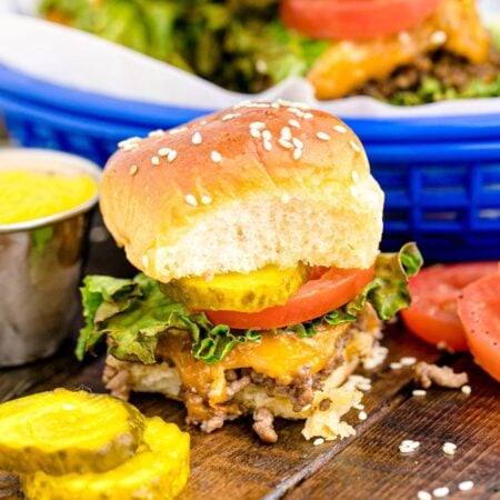 Classic Cheeseburger Slider on table wit hsome sliced pickles and tomatoes in front of the burger
