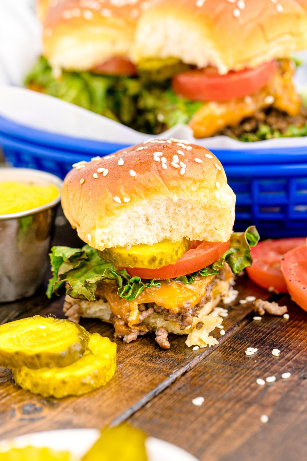 Classic Cheeseburger Slider on table wit hsome sliced pickles and tomatoes in front of the burger 