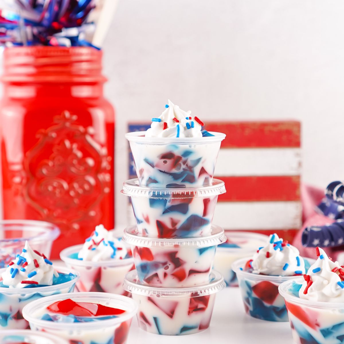 Red White and Blue Jello Shots in containers spread out on table with red white and blue decor in the background 