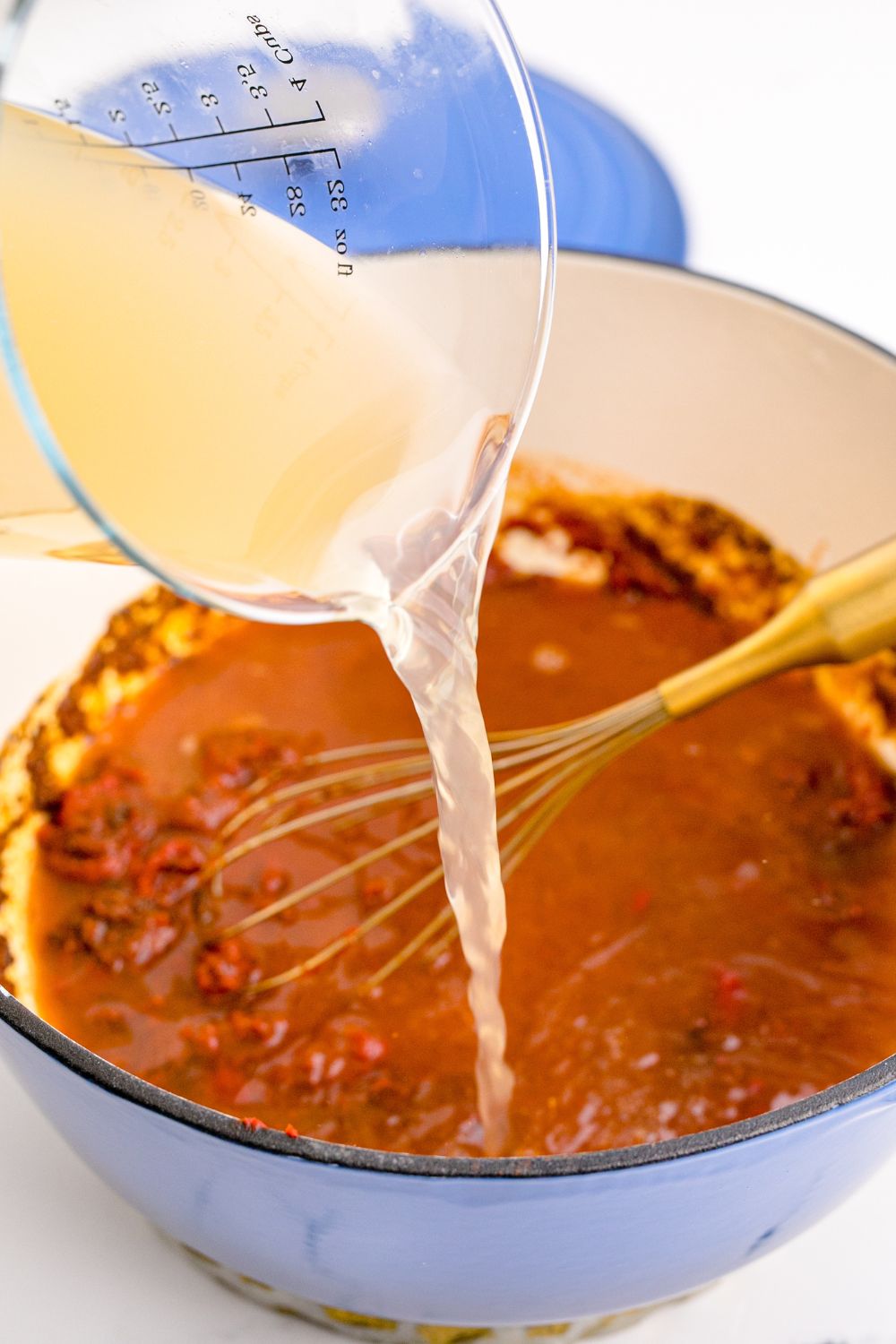 Homemade Enchilada Sauce being made with stock being poured into pan with tomato mixture in it