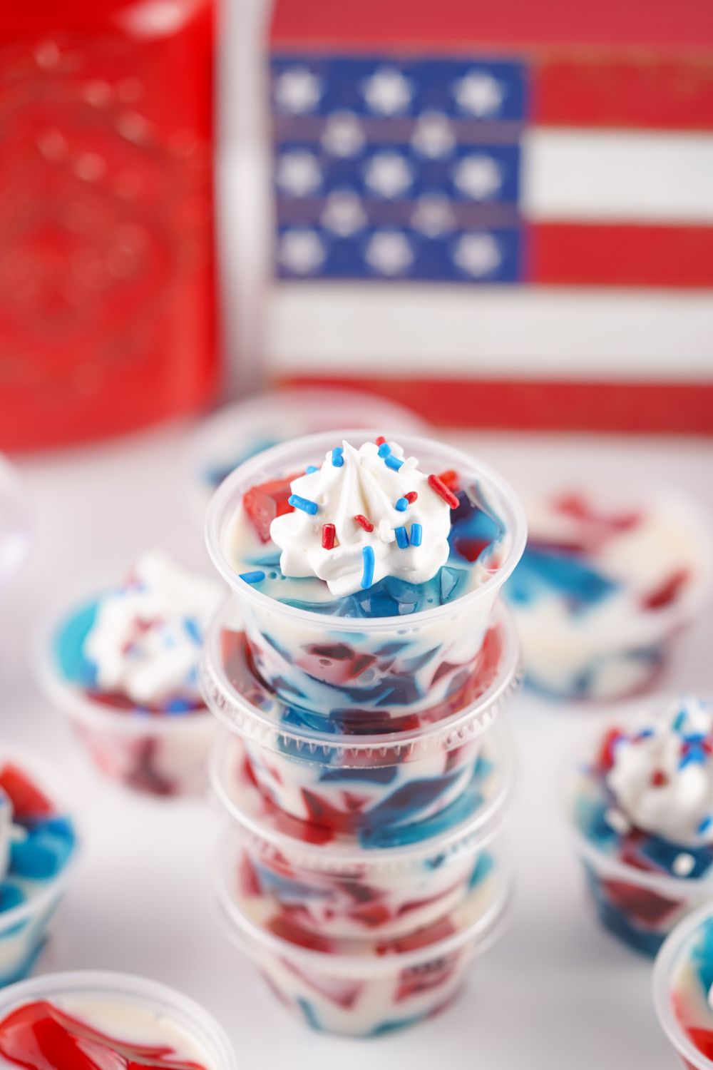 Red White and Blue Jello Shots stacked up with the top one without lid and whipped cream and sprinkles on top 