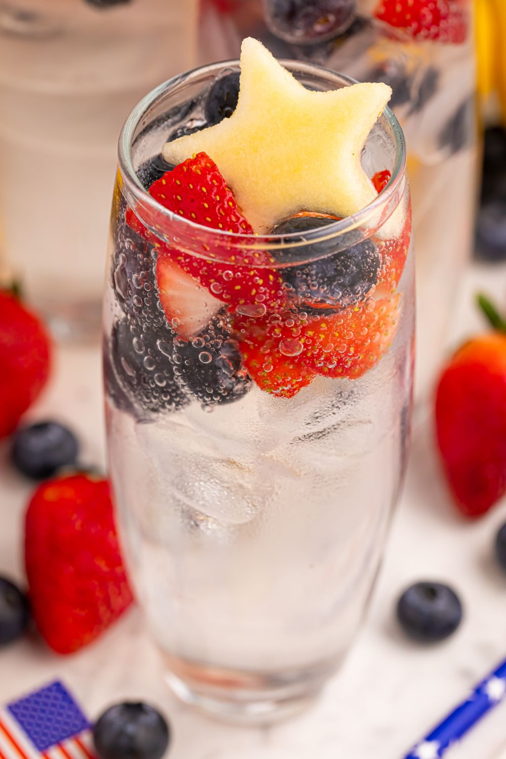 glass full of Patriotic Sparkling Lemonade and topped with fruit sitting on table 