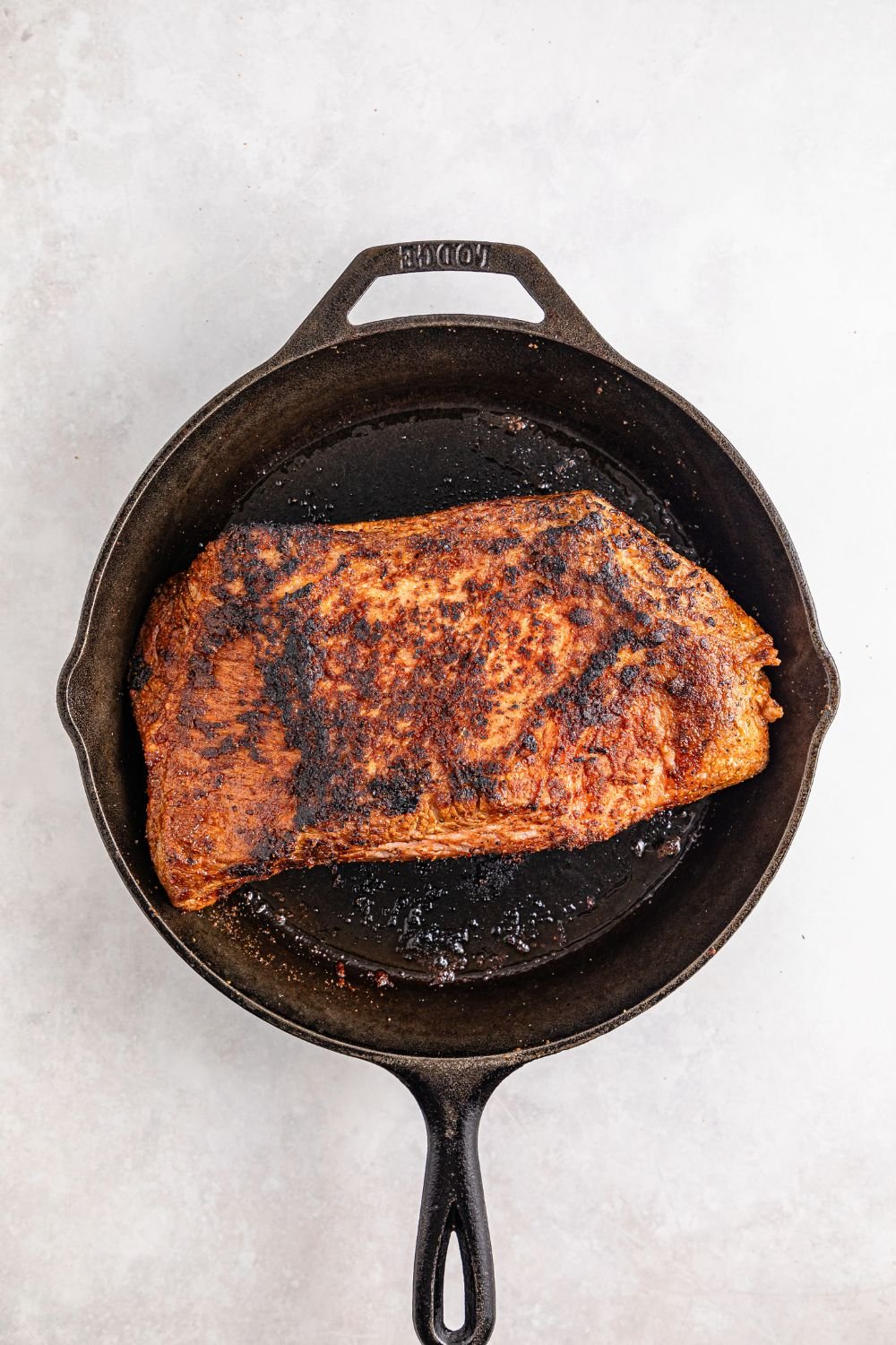 cast iron skillet with a seared brisket in the pan 