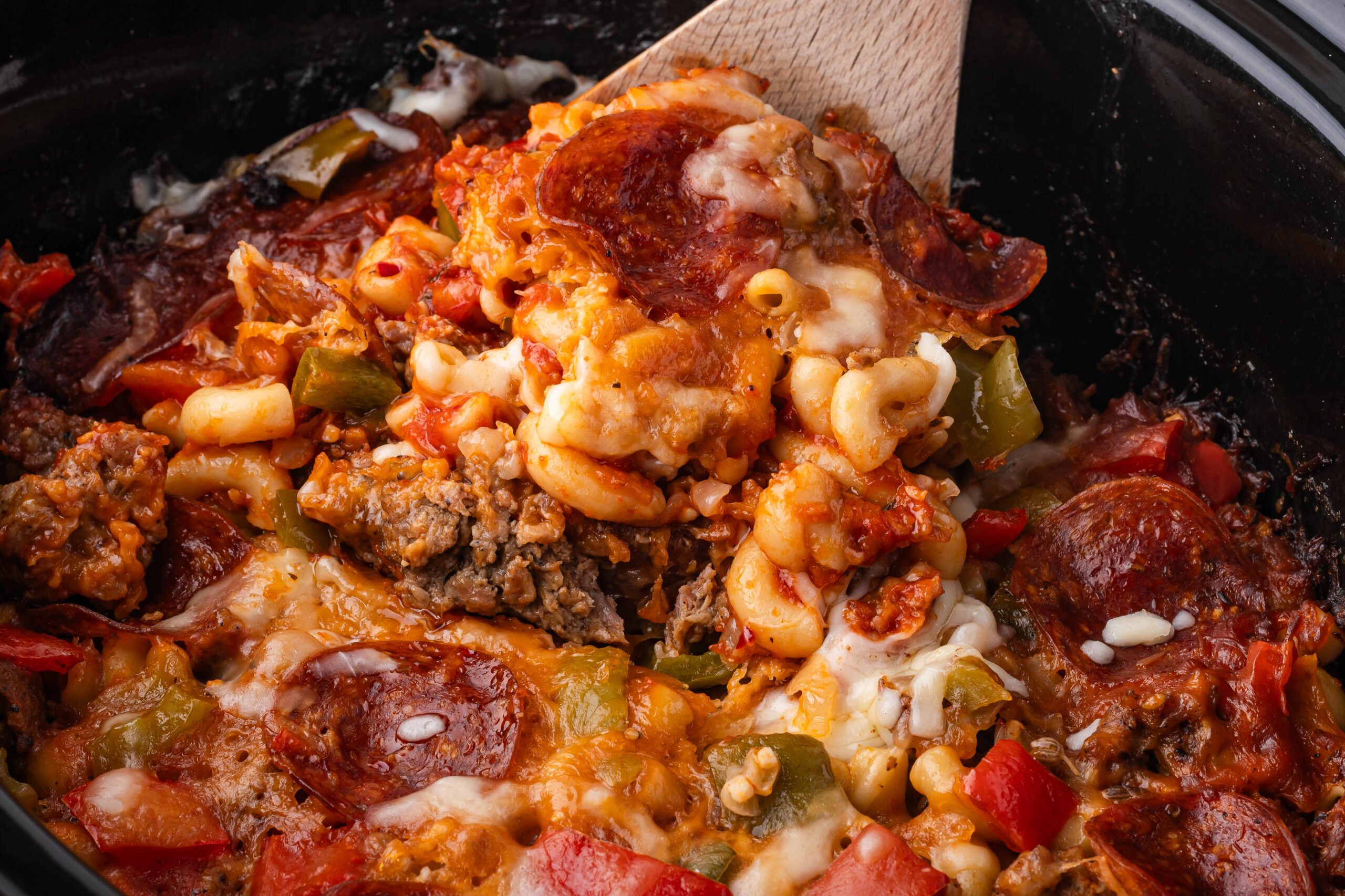 spoon lifting up some of the Slow Cooker Pizza Casserole  out of the crock pot 