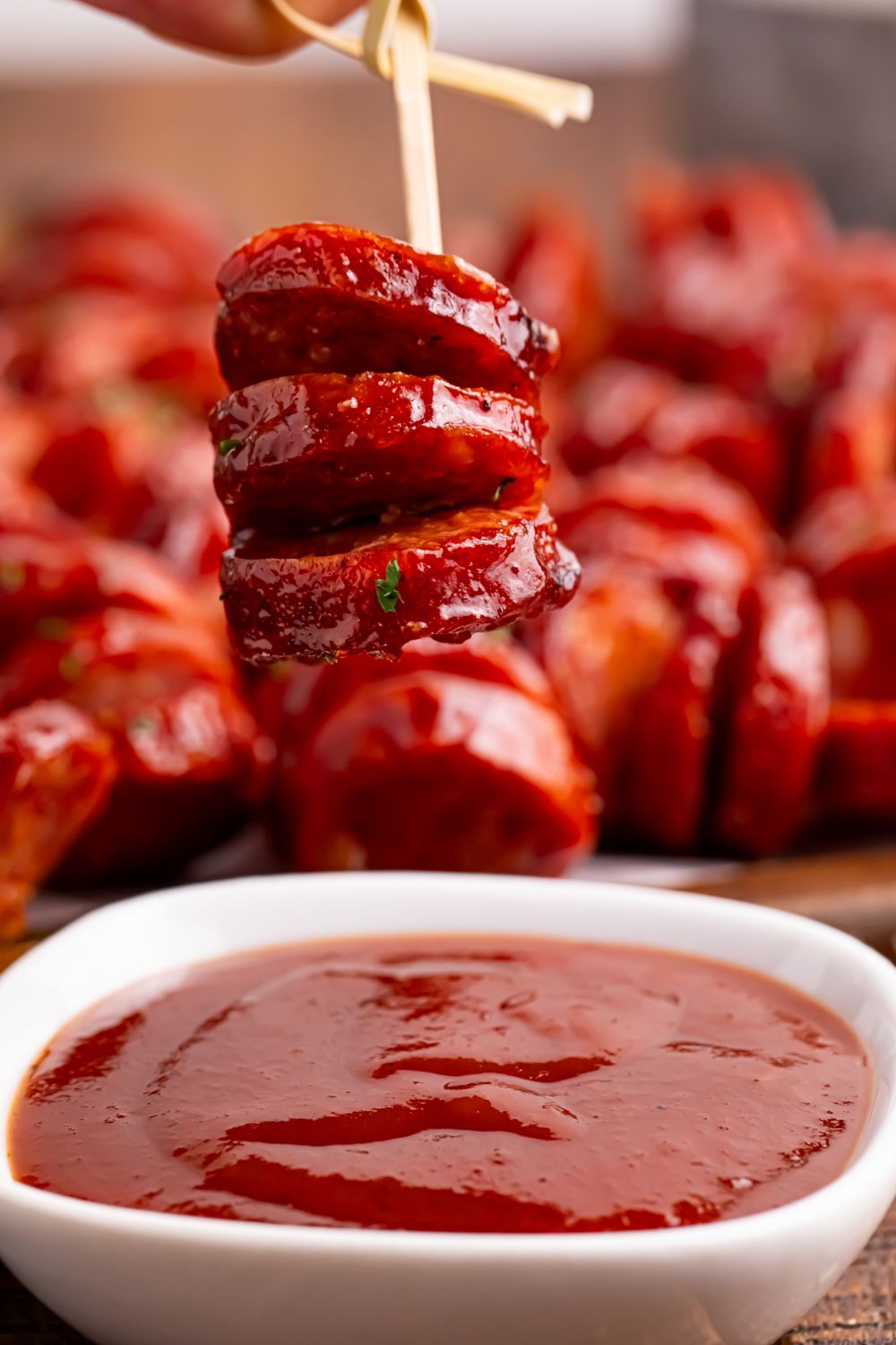 BBQ Hasselback Smoked Sausages being held above a bowl of sauce on table 