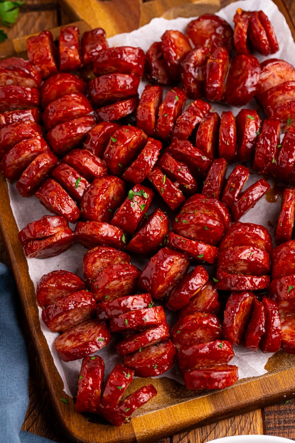 BBQ Hasselback Smoked Sausages on cutting board with parchment paper under the meat 