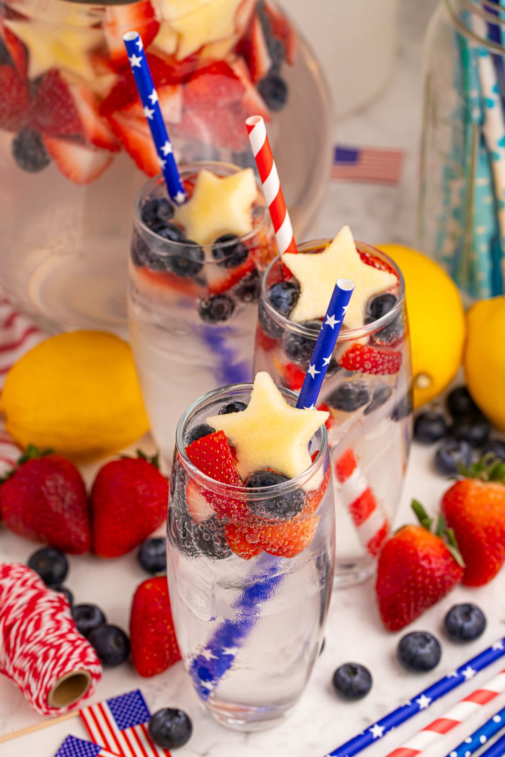 Patriotic Sparkling Lemonades in glasses on table with lemons, strawberries, and blueberries around the table 