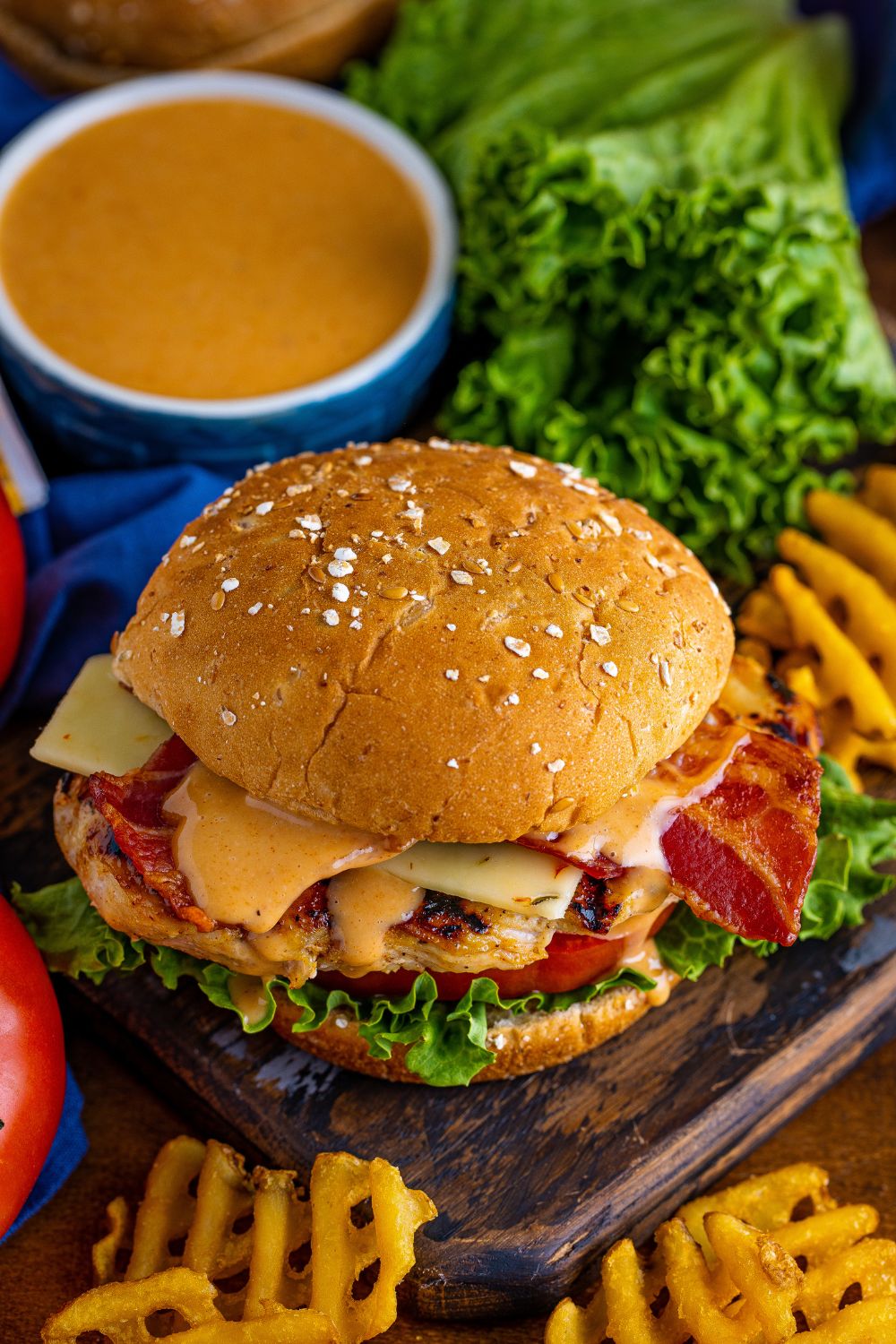 Chick Fil A Grilled Chicken Sandwich on wooden platter with fries around it and a dipping sauce in bowl 