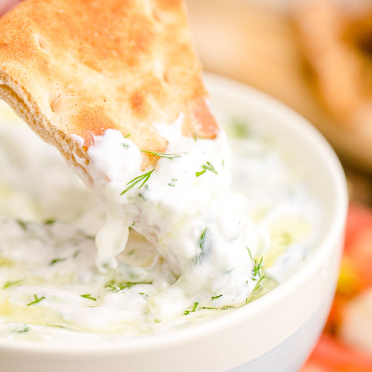 Tzatziki Sauce in a bowl with a pita dipped in sauce