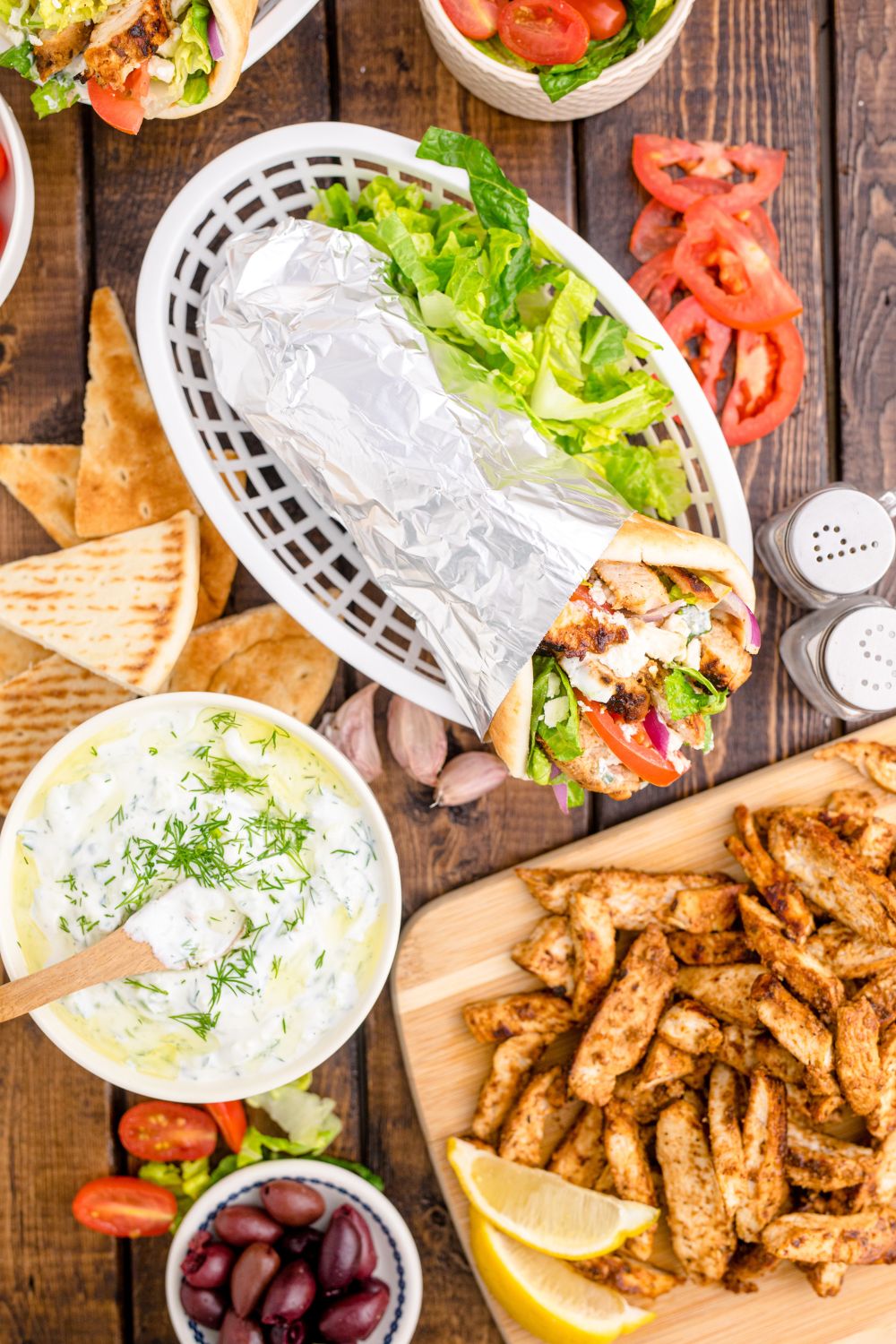 basket with gyros, bowl of tzatziki sauce in bowl, plate of diced chicken and more on table