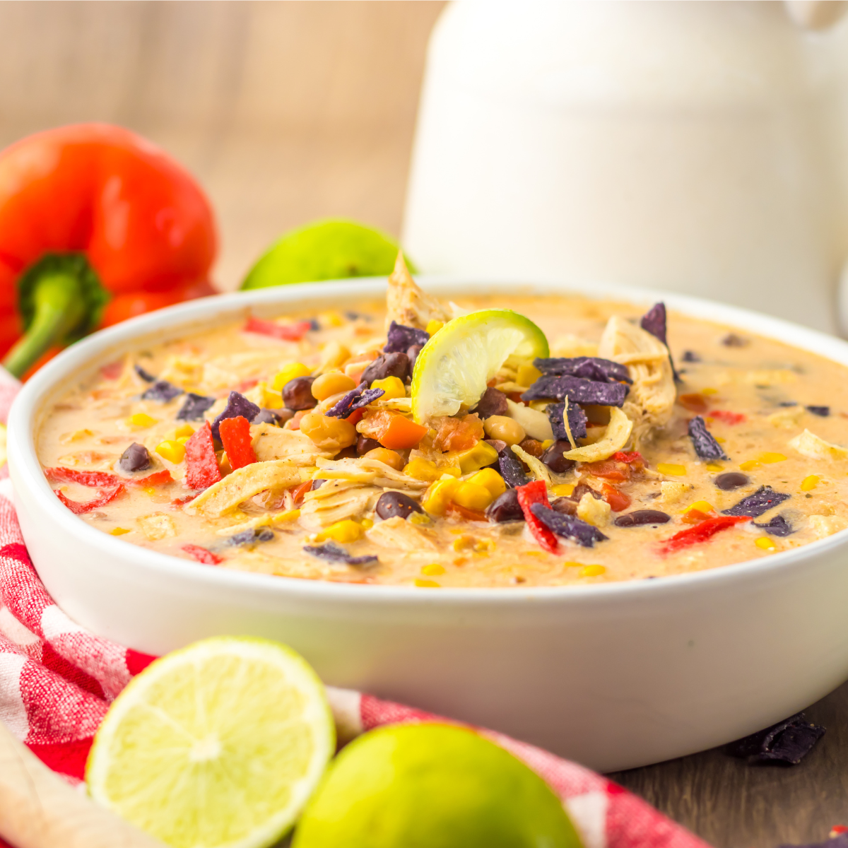 Close up side view of a bowl of tortilla soup topped with tortilla chips, corn, and beans. 