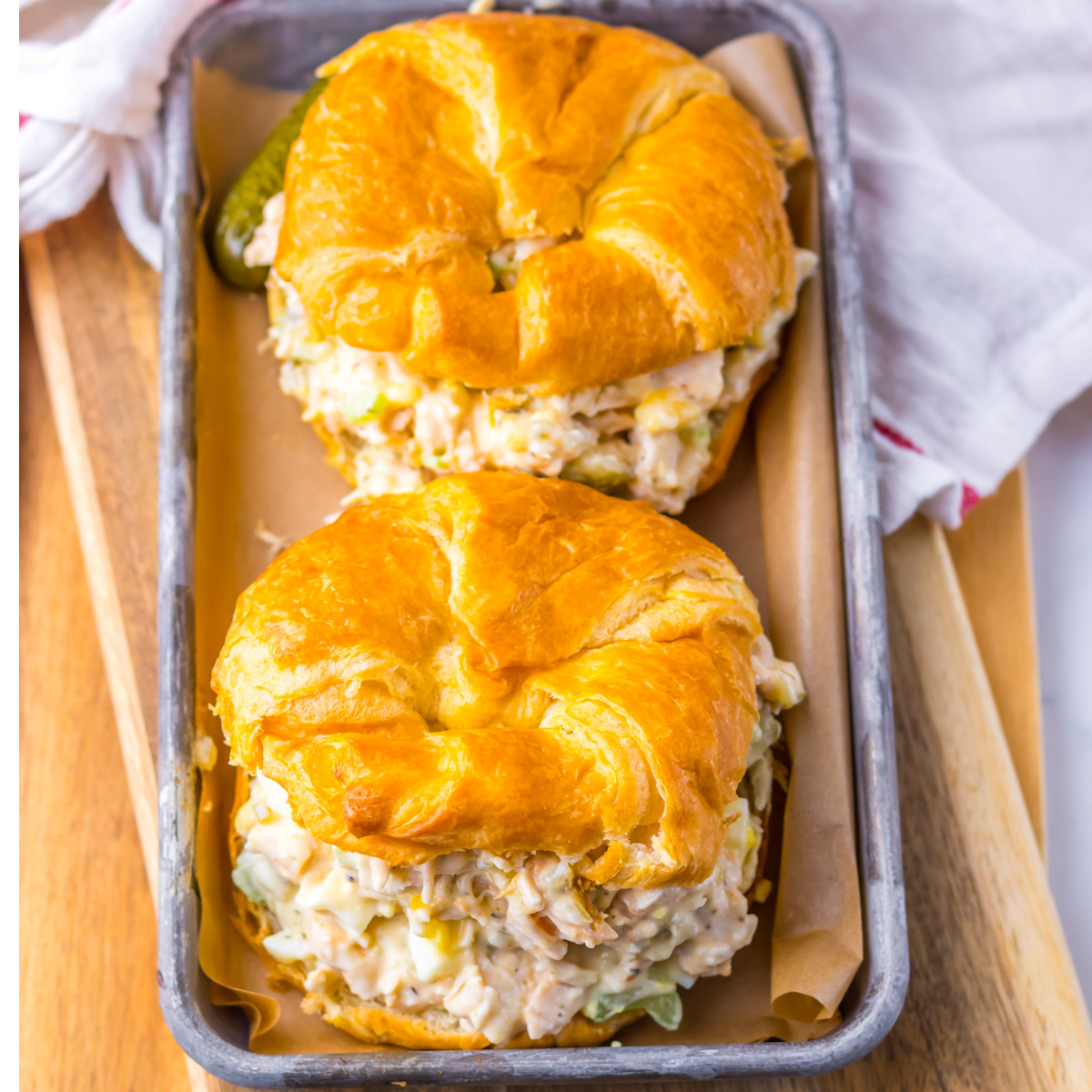 Overhead shot of chicken salad on a white croissant on a tin tray.  
