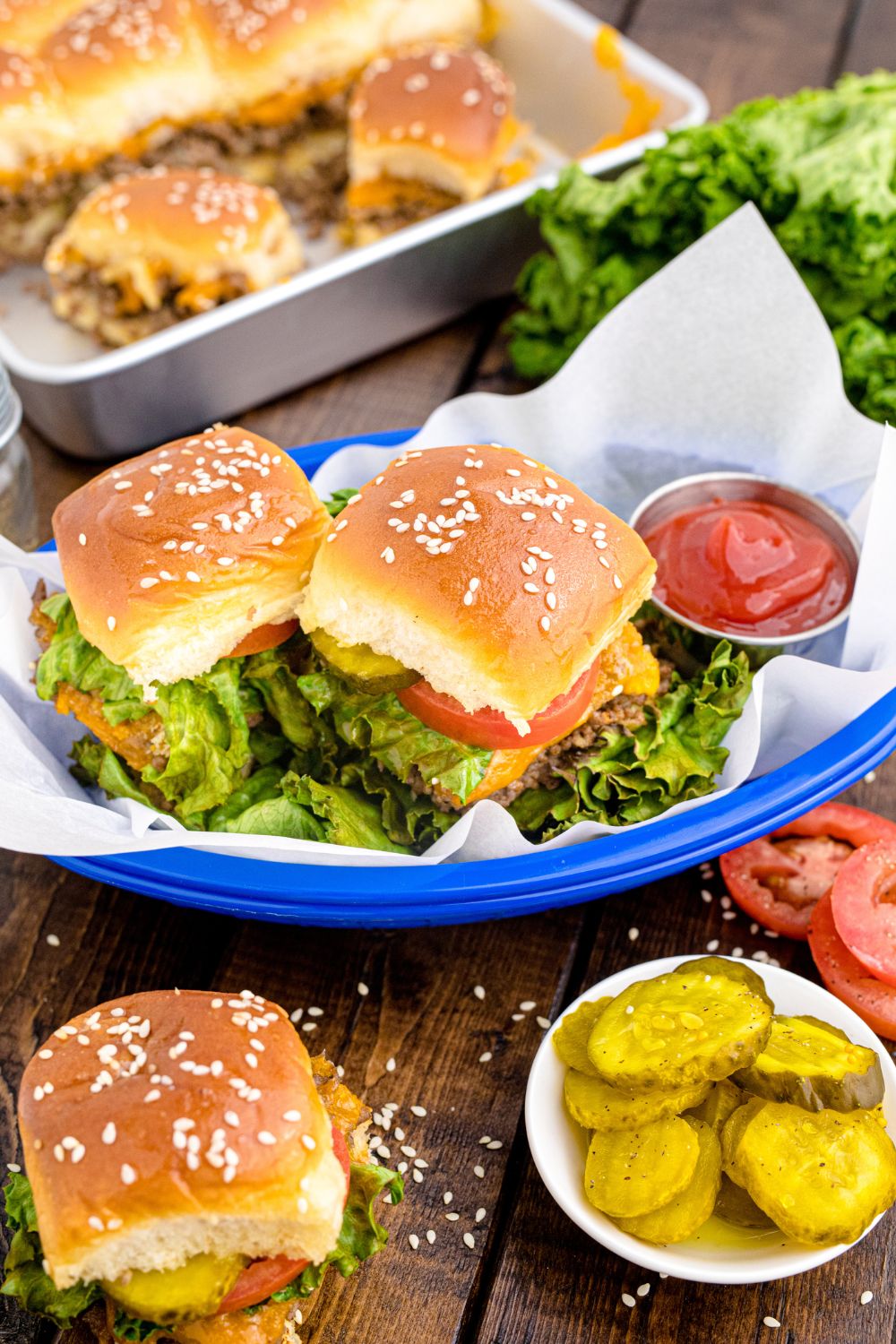 Classic Cheeseburger Sliders spread out on table in pan and in baskets with condiments and burger toppings around the pan 