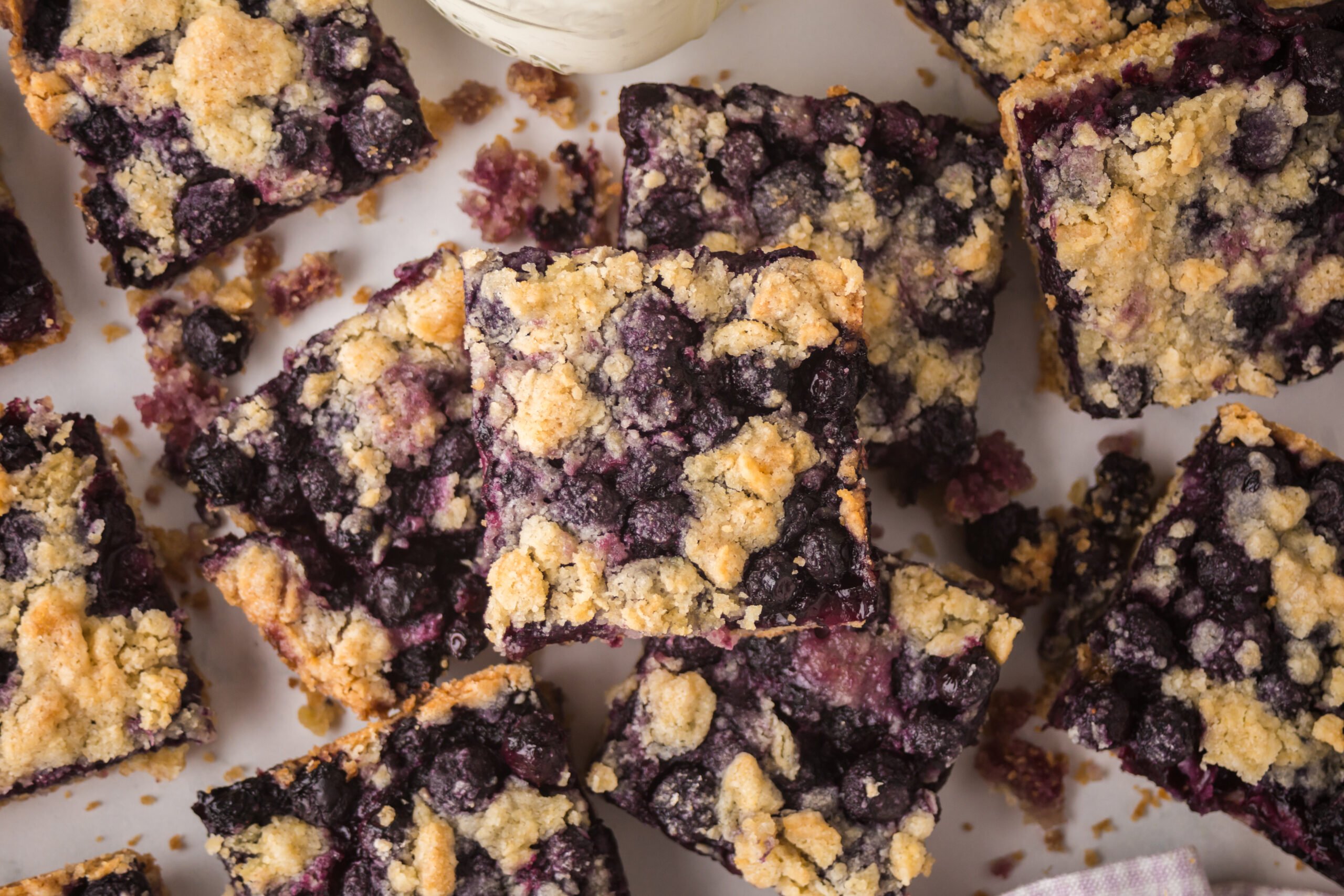 blueberry crumble bars stacked on a white table 