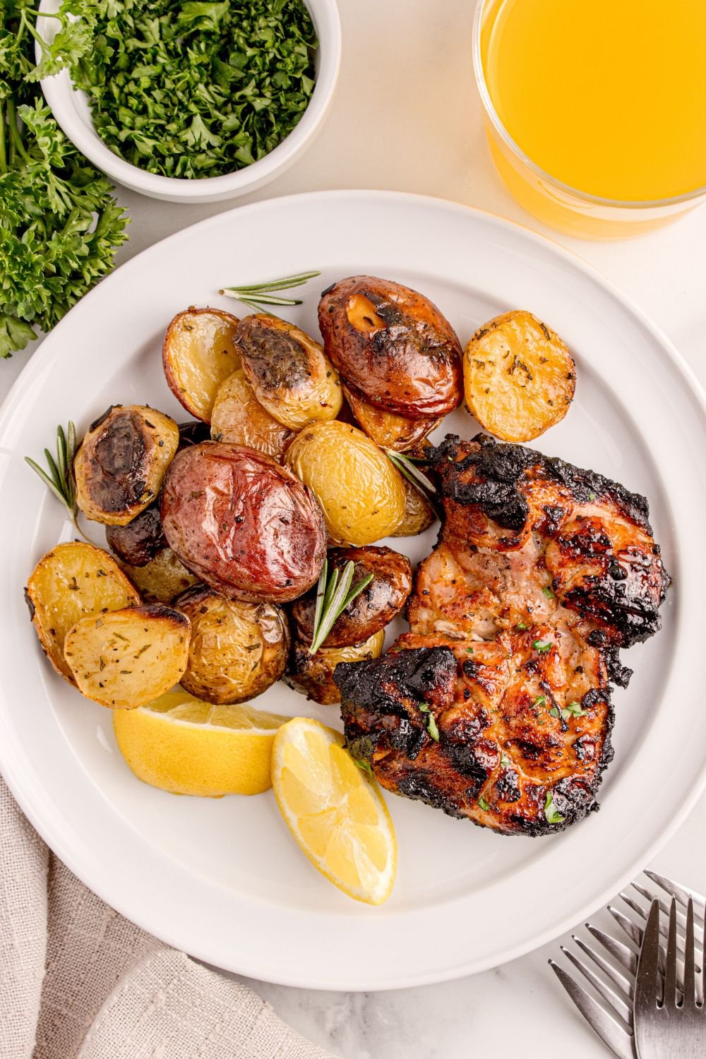 Grilled Chicken Thigh on plate with some lemon wedges and roasted potatoes