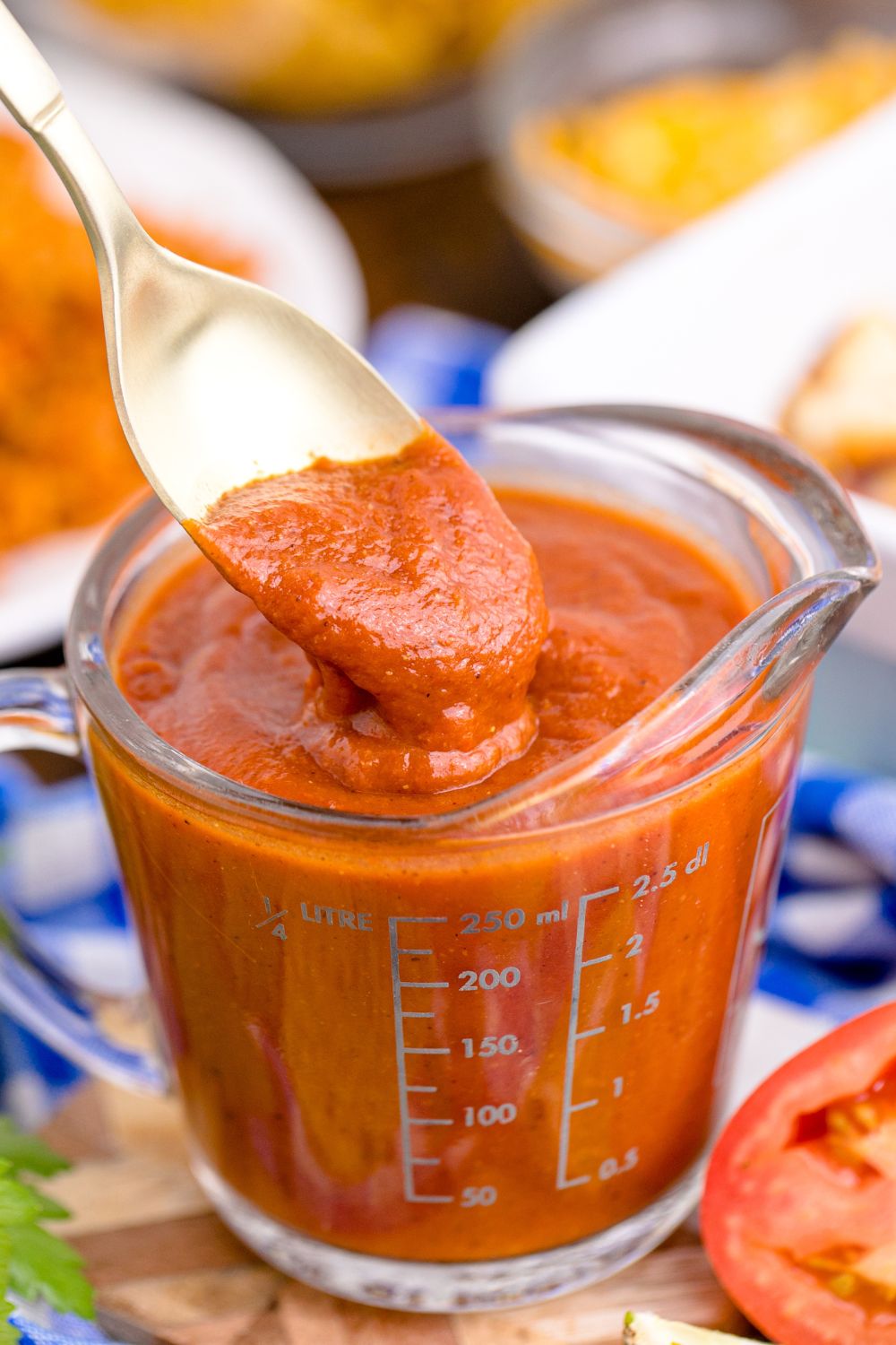 measuring cup with homemade enchilada sauce in it with a spoon lifting out some of the sauce
