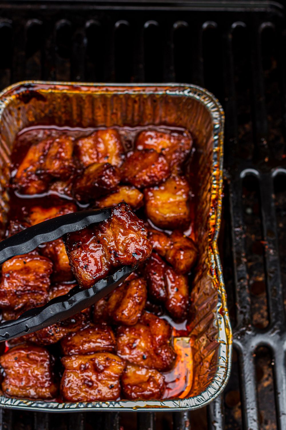 Smoked Pork Belly Burnt Ends in a foil container on the grill 