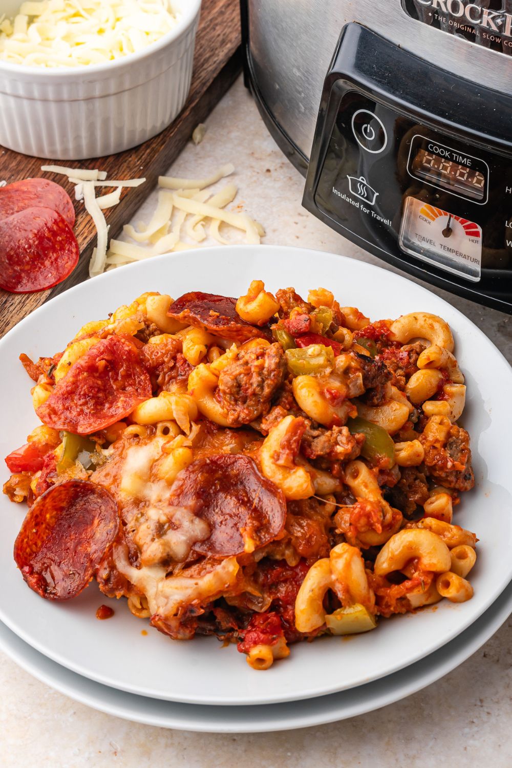 Pizza Casserole is on a plate with a slow cooker behind it on table 