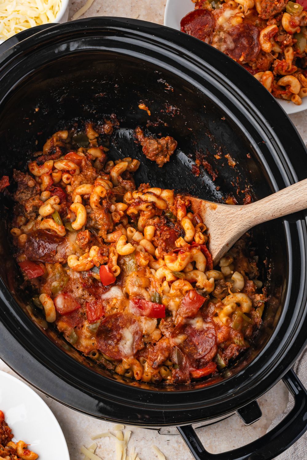 overhead Slow Cooker Pizza Casserole in a slow cooker on table with a spoon to side of container 