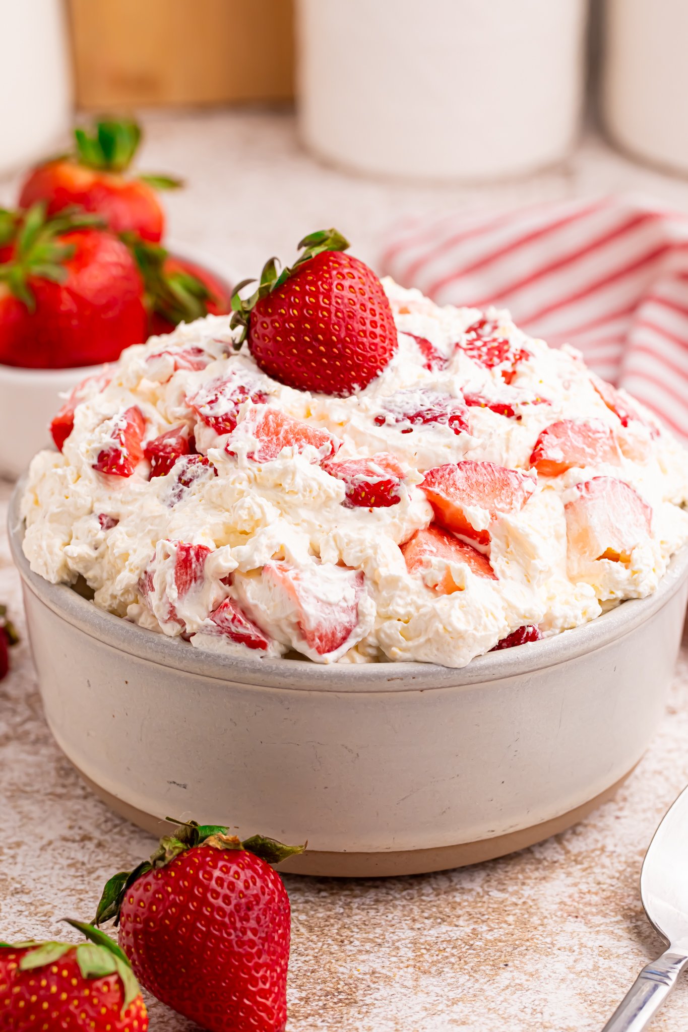side shot of Overhead view of the strawberry cheesecake salad in a white bowl with a fresh strawberry on top. 