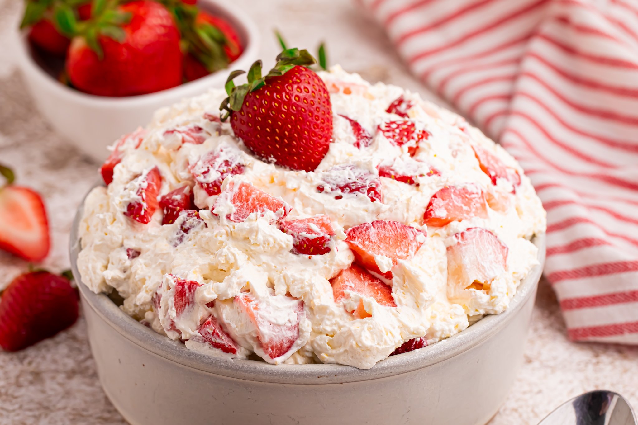 side shot of the strawberry cheesecake salad in a white bowl with a fresh strawberry on top. 