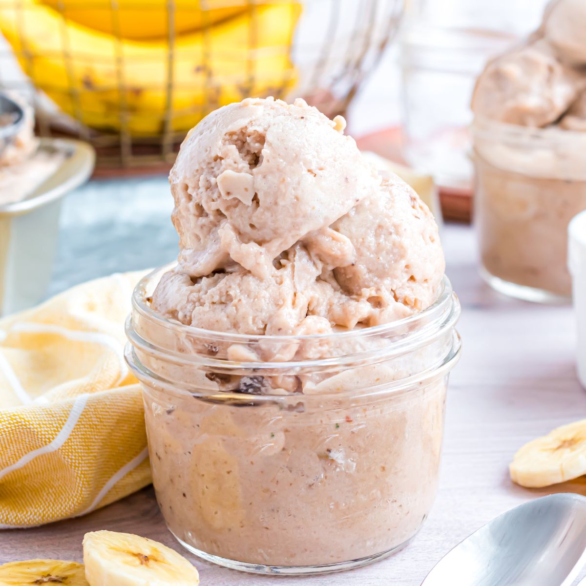 Banana Ice Cream in a glass bowl on table with slices of bananas around table 