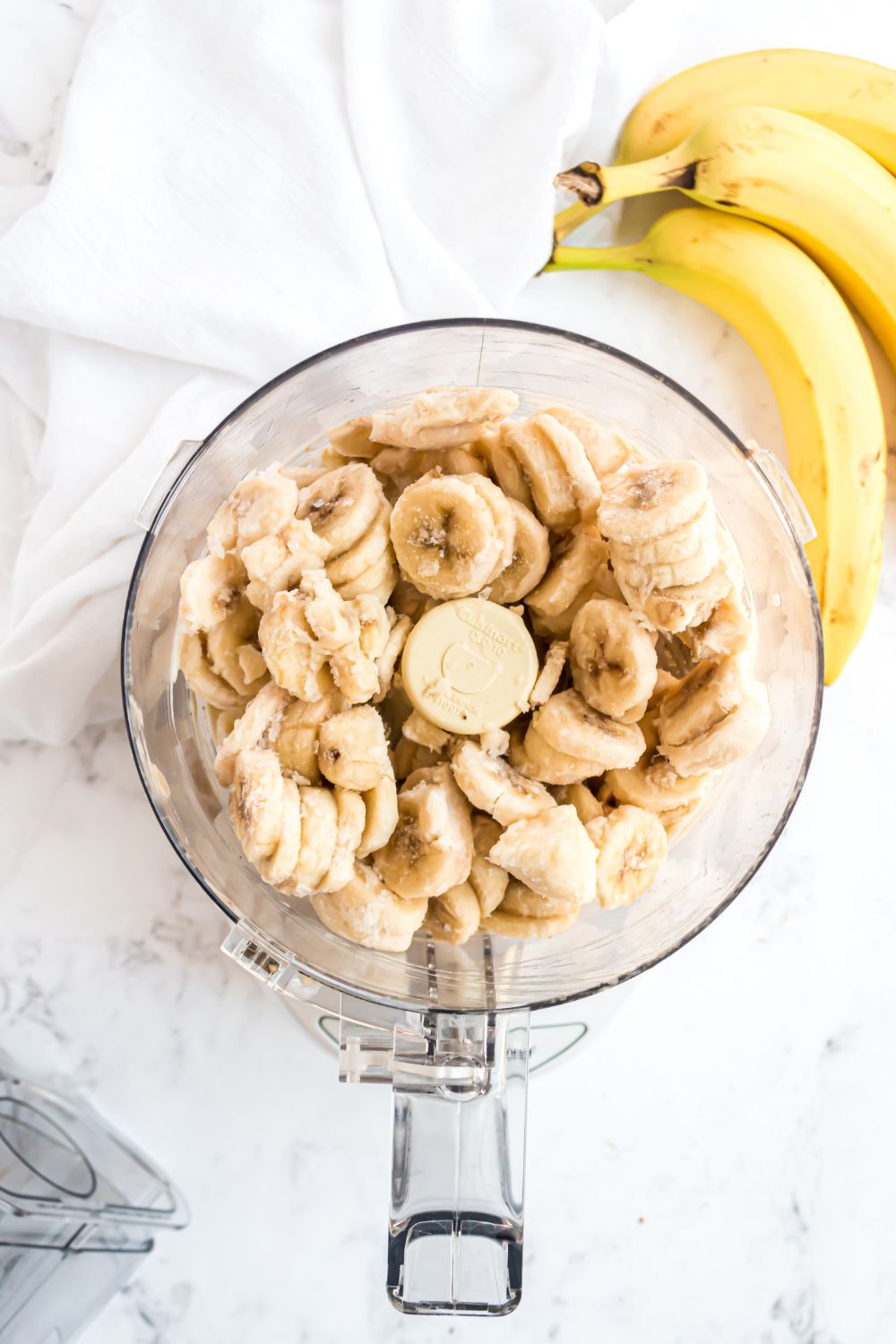 frozen bananas in a food processor with bananas to side for making Banana Ice Cream