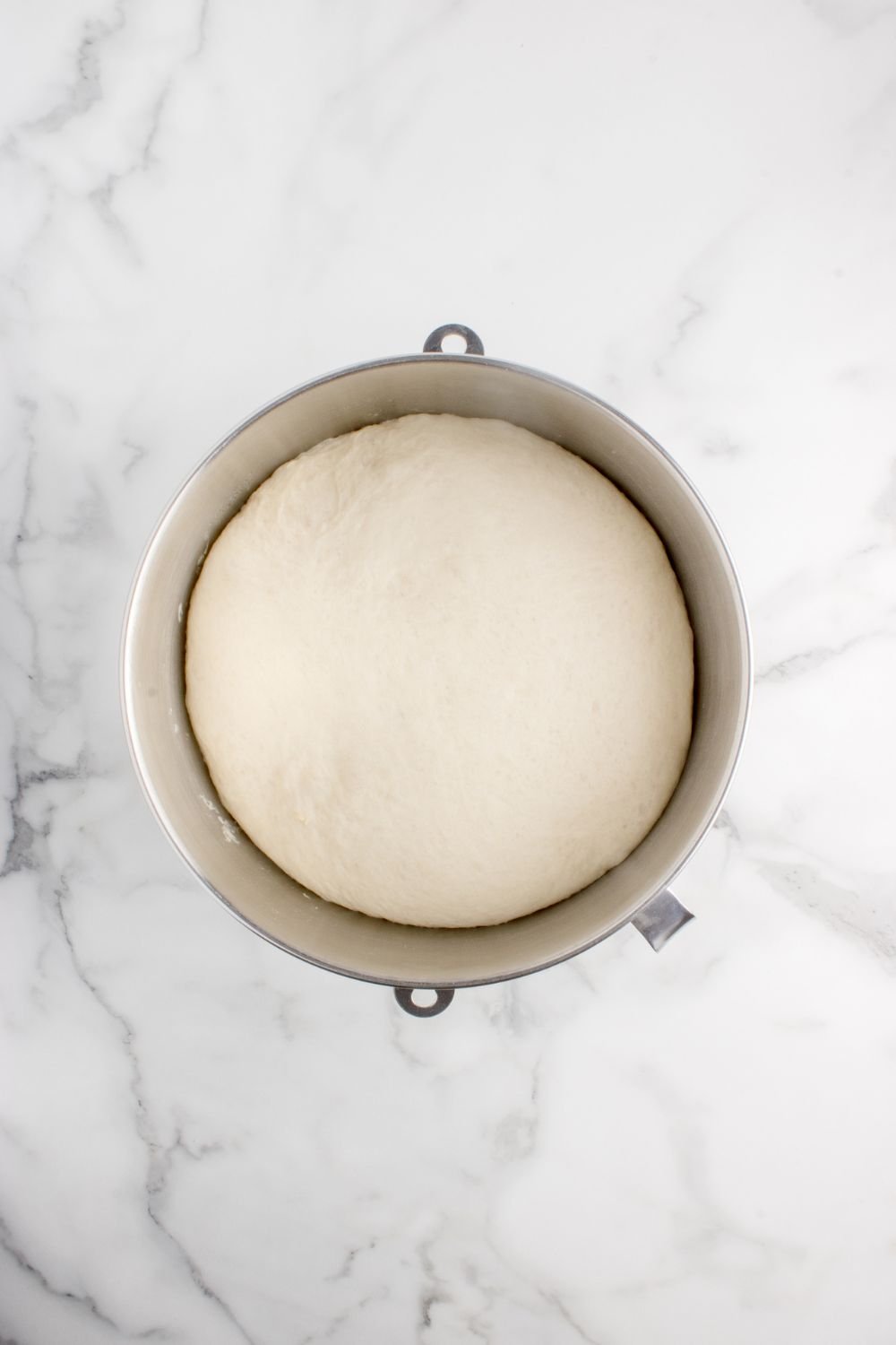 risen dough in a metal bowl on table 