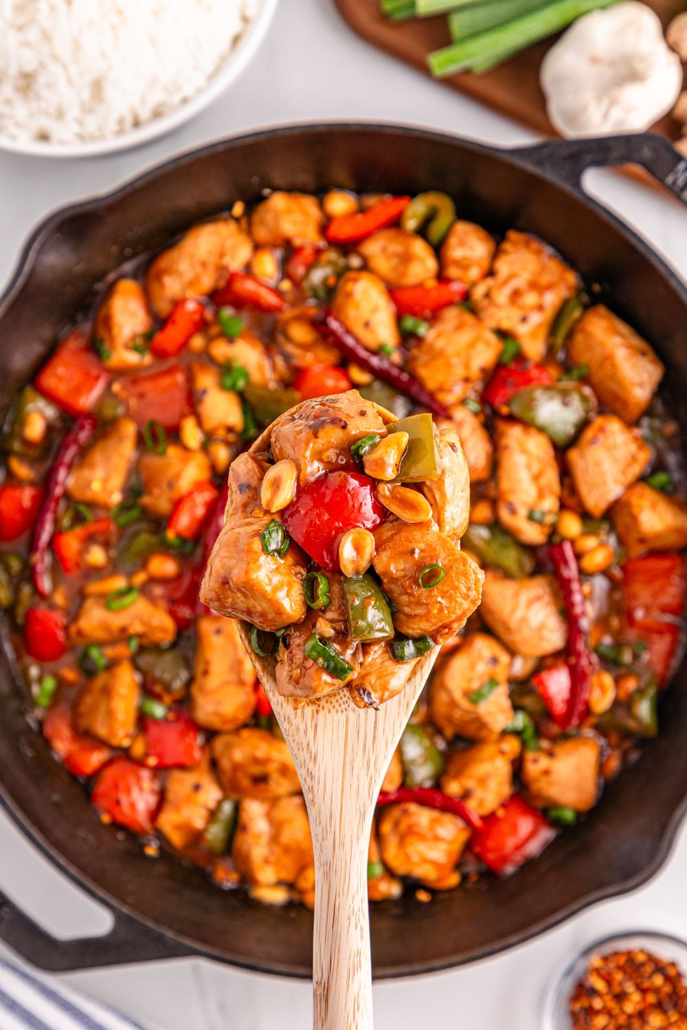 Better Than Takeout Kung Pao Chicken in a skillet with a wooden spoon scooping out of it 