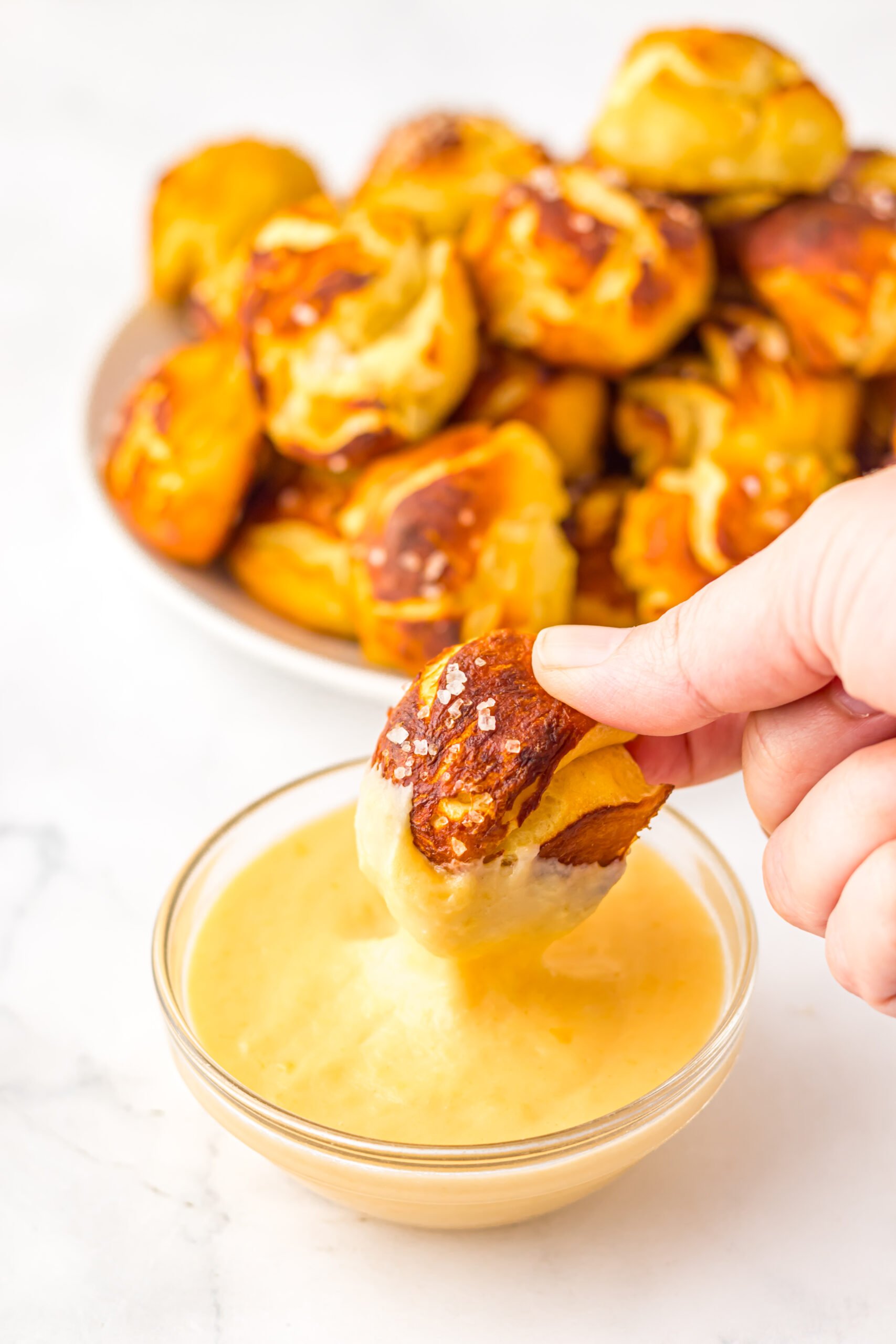 Easy Biscuit Pretzel Bites with a hand dipping one into the Cheese Sauce 