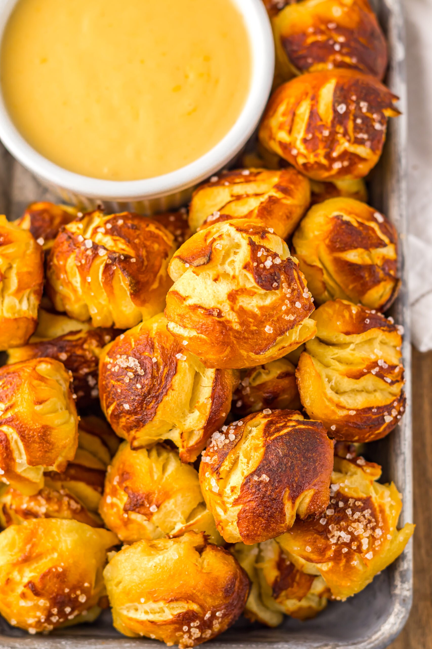 Easy Biscuit Pretzel Bites with Cheese Sauce on a tray sitting on table with a glass to the side 