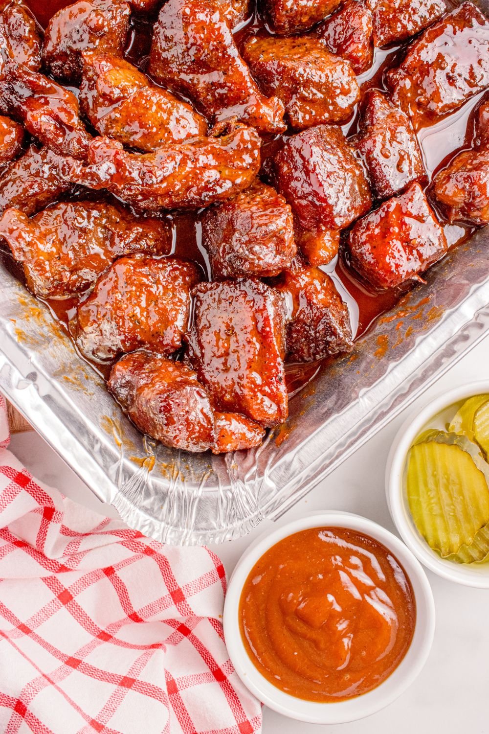 Chuck Roast Burnt Ends in a foil tray with sauces and pickles to side of container 