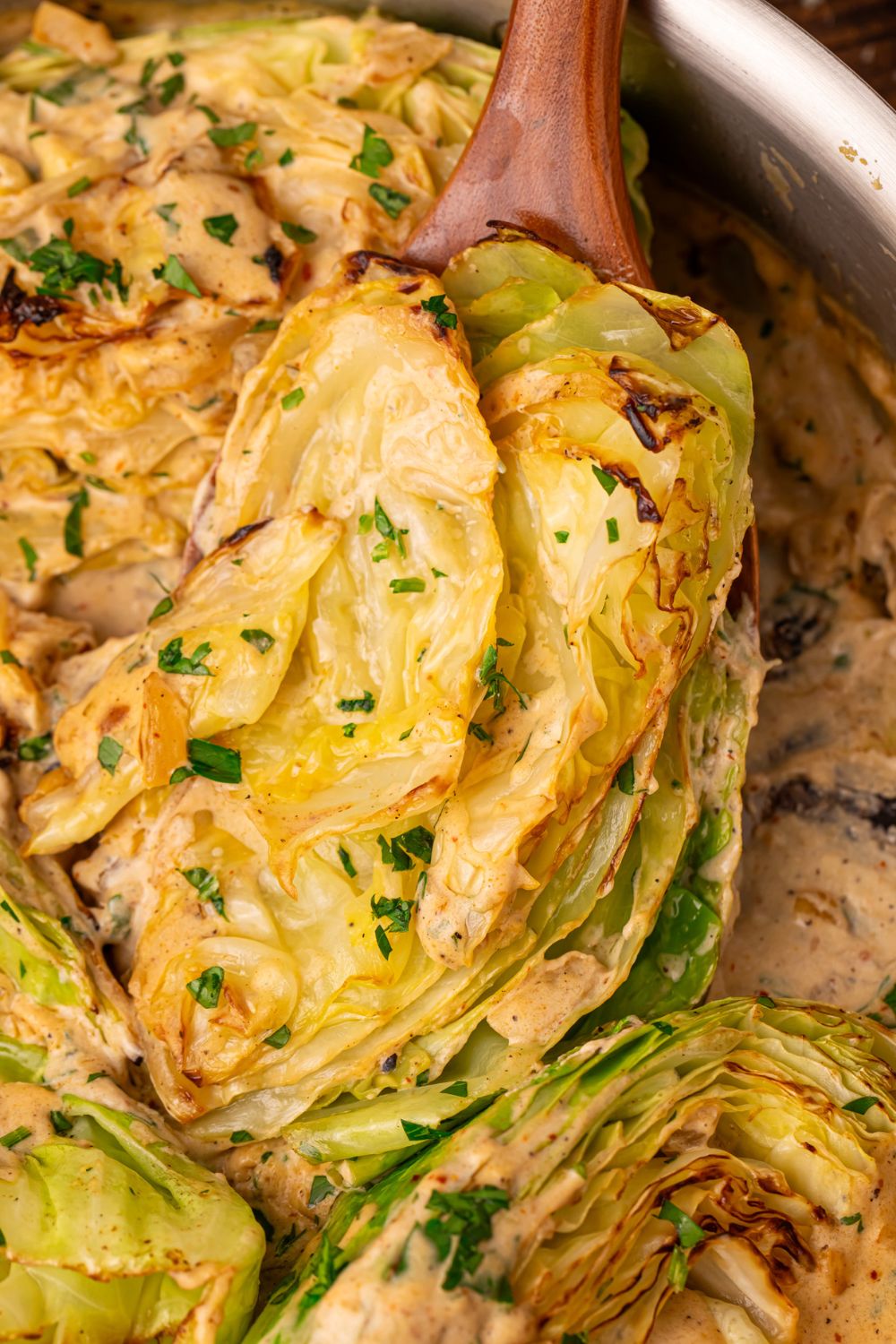 Creamy Garlic Parmesan Cabbage in a skillet with one being lifted out with a spoon 