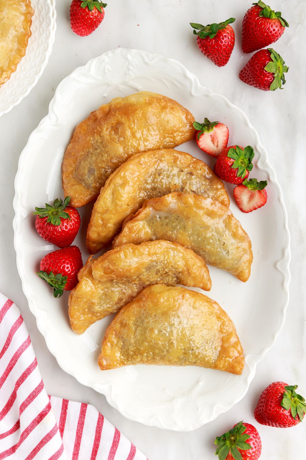Deep Fried Strawberry Cheesecake Pies on a tray with strawberries scattered around the table with a red striped towel to side 