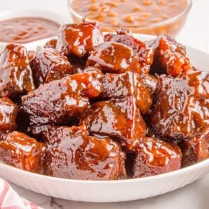 Chuck Roast Burnt Ends in a bowl sitting on table with sauce and beans in background