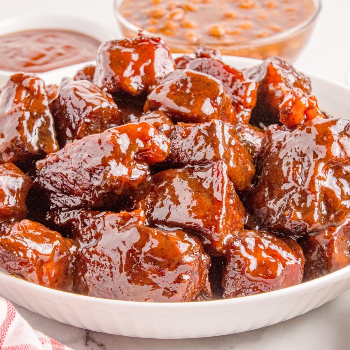 Chuck Roast Burnt Ends in a bowl sitting on table with sauce and beans in background