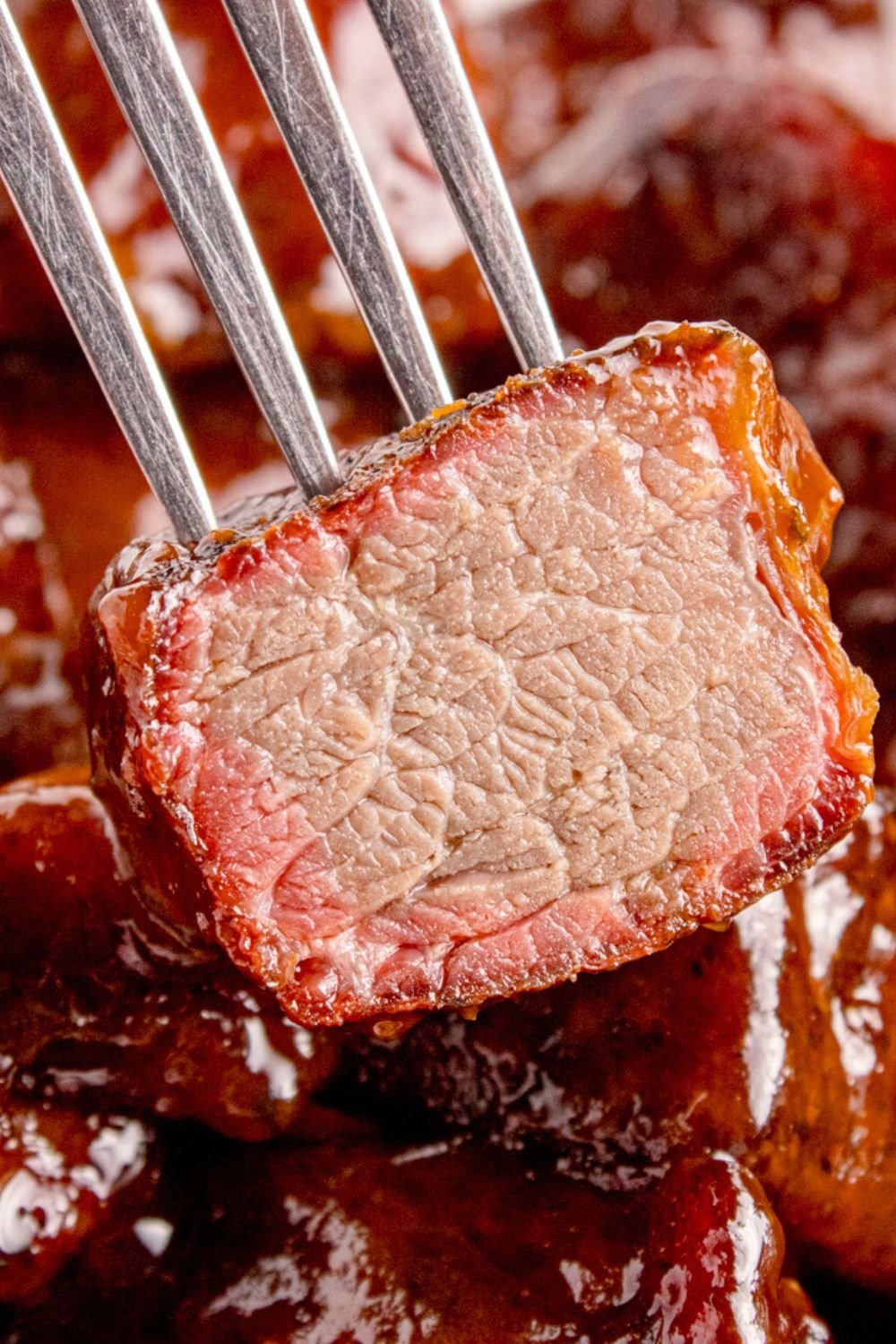 fork with a piece of burnt end that is cut in half to show the meat on it 